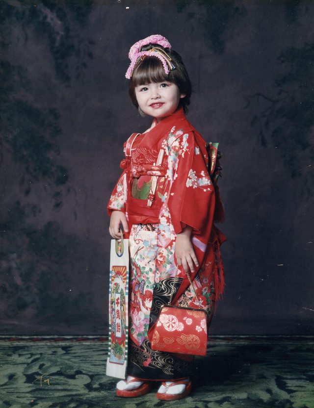 Saya as a young child in a red floral kimono for Shichi-Go-San, holding a chitose-ame candy bag and a small red purse.